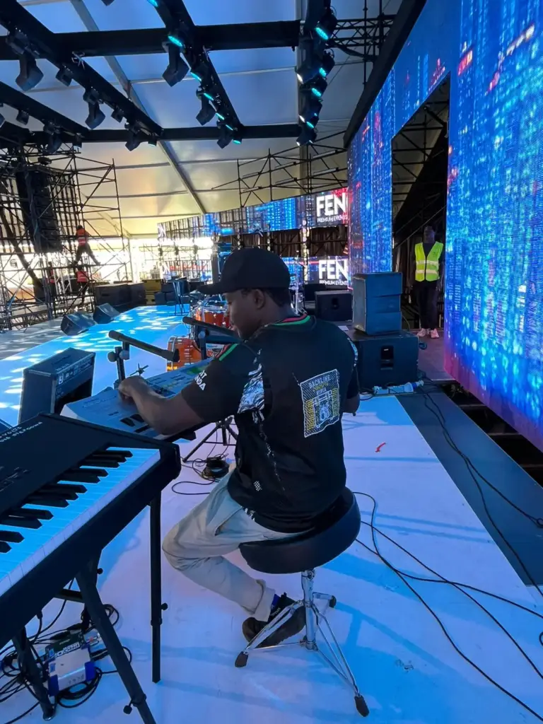 Keyboard player sound-checking at a keyboard stand in front of a blue LED wall on a tented stage in Kenya