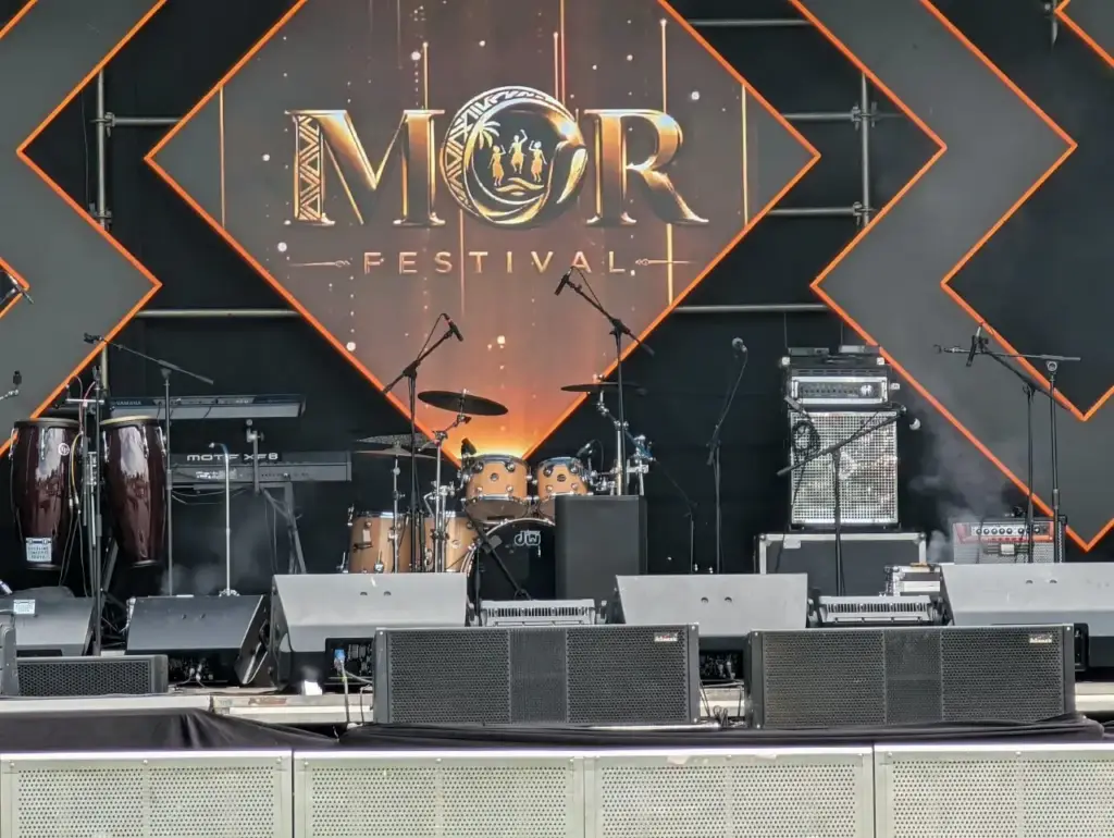 MOR Festival stage front with wedge monitors and front speakers below the backline and festival backdrop in Kenya