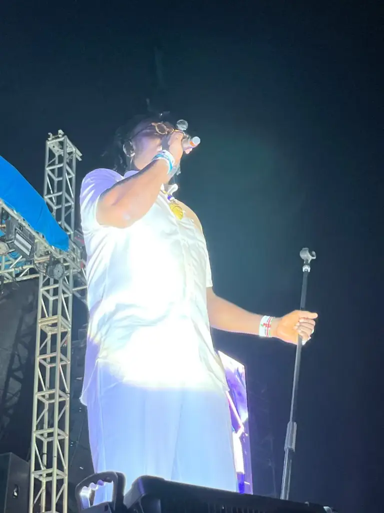 Performer in white singing into a handheld microphone on an outdoor stage in Kenya