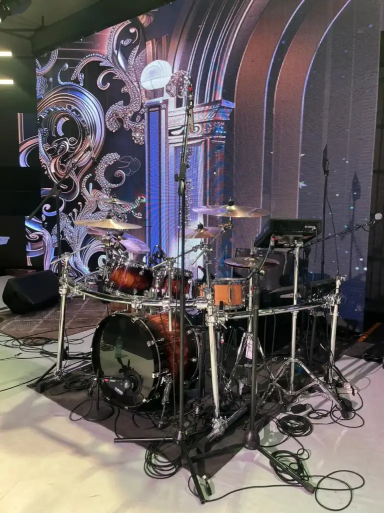 Burst finish drum kit on a chrome rack with a percussion pad, set in front of an ornate silver backdrop in Kenya