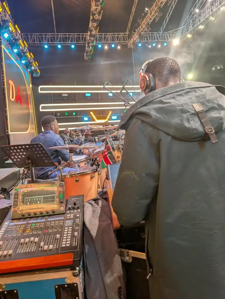 Monitor engineer working stage-side beside the house drum kit under the lighting truss at Rhema Feast 2026 in Nairobi