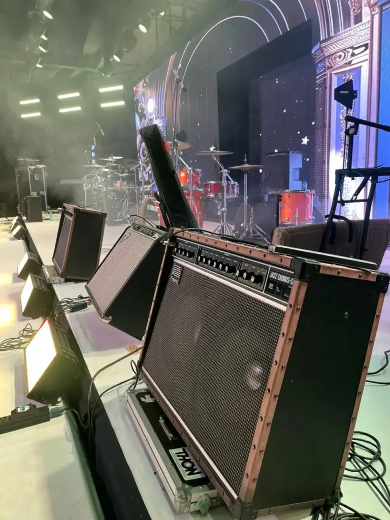 Roland Jazz Chorus guitar amplifier on its flight case at the stage edge, with a red drum kit and ornate LED set behind, in Kenya