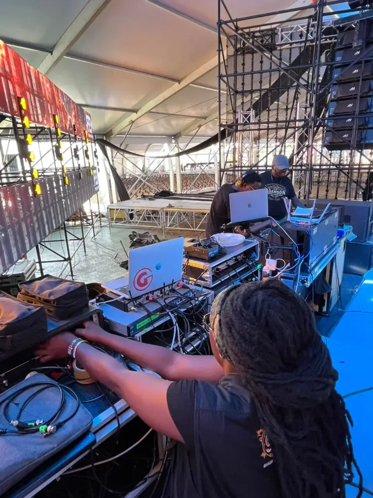 Technician working at a side-stage rack and laptop with line array speakers flown in the marquee behind, in Kenya