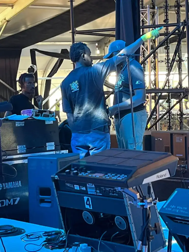 Crew at the side-stage position beside a Yamaha DM7 console case, with a Roland sampling pad in front, in Kenya