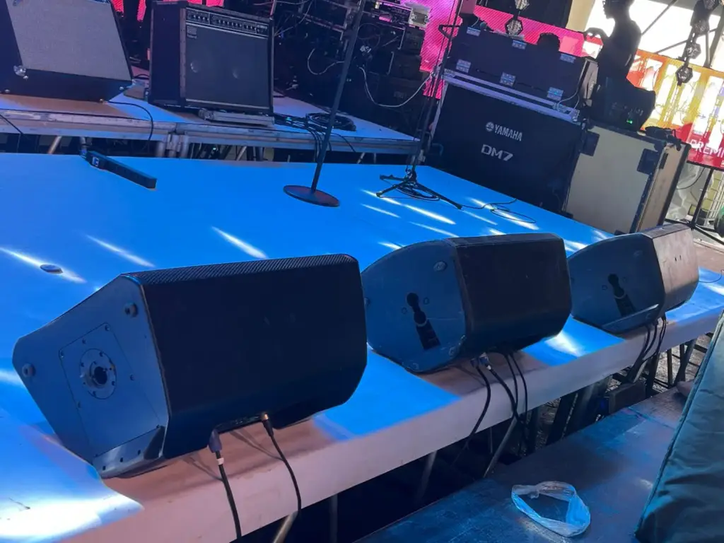 Three stage wedge monitors lined up along the stage lip, with a Yamaha DM7 console case behind, in Kenya