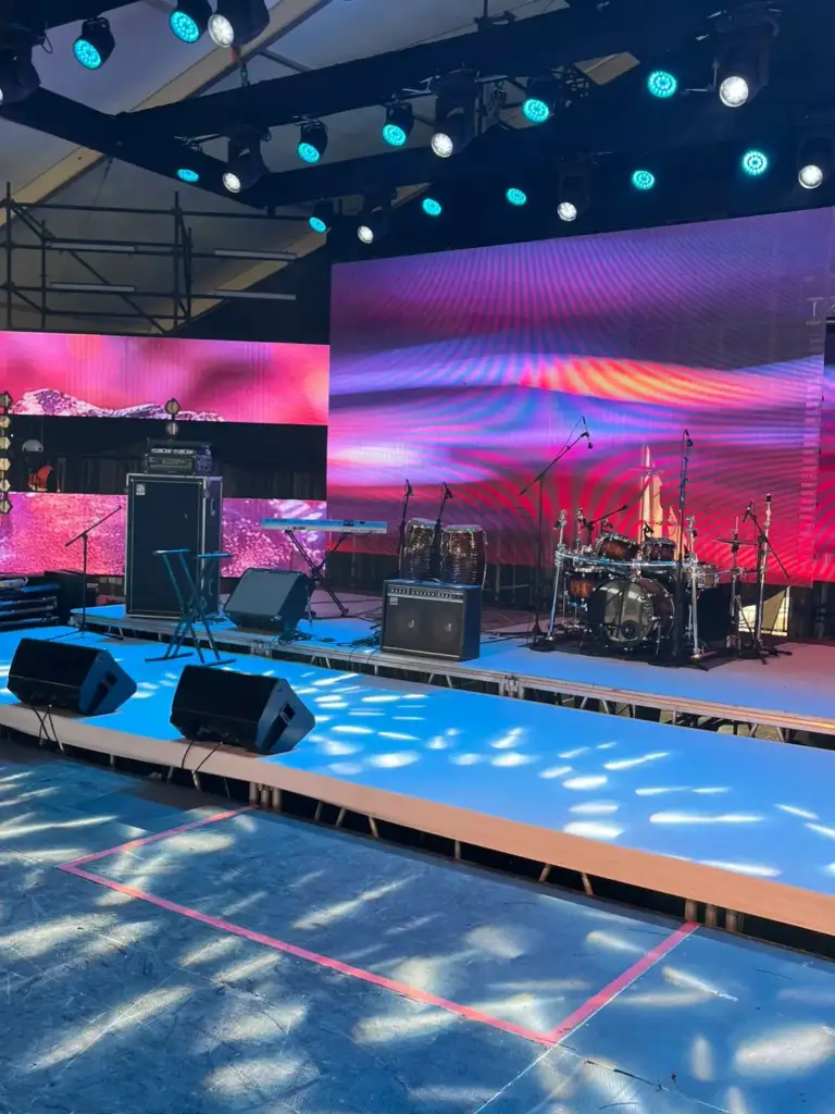Large tented stage with pink LED walls, a drum kit, congas, amplifiers and wedge monitors set before a show in Kenya