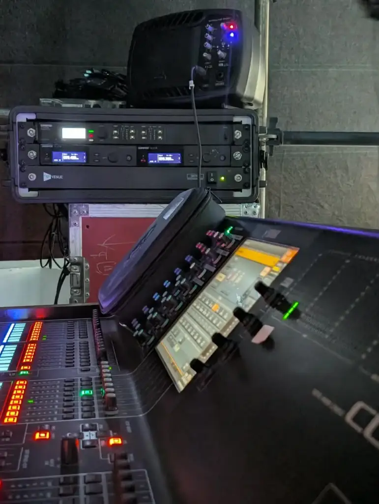 Rack of wireless microphone receivers above a digital mixing console beside the stage in Kenya